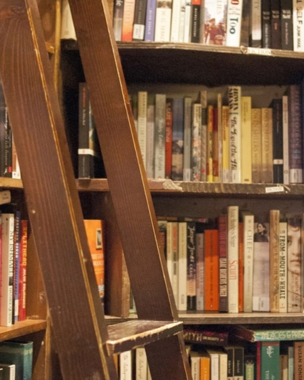 A wooden library ladder leaning against floor-to-ceiling shelves of books